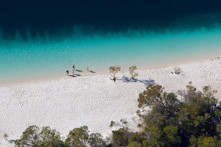 Four-wheel-drive travellers beside the turquoise water and white sand of K'gari